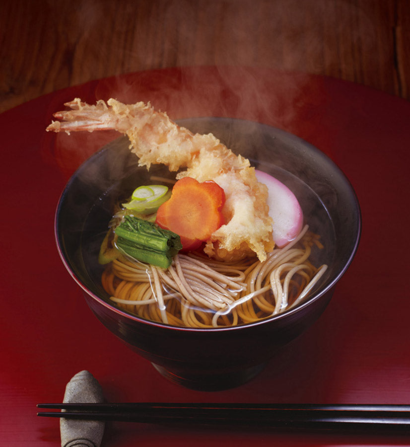 Bowl of Kayanoya soba noodles with tempura on a red table
