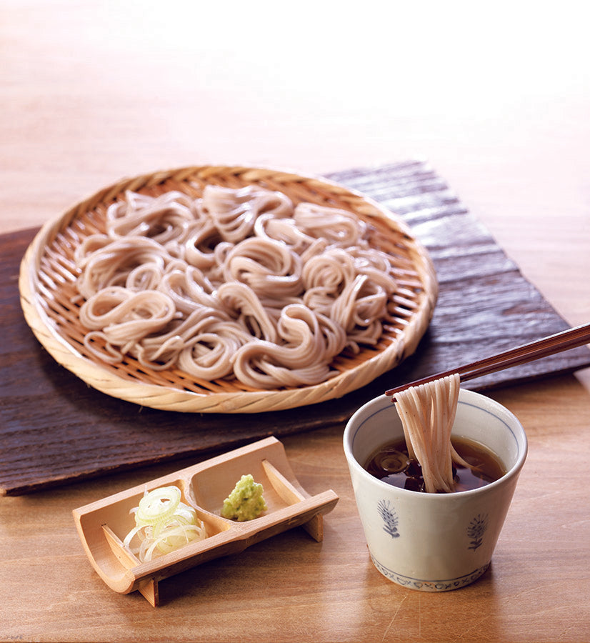 Kayanoya Soba noodles in a bowl with dipping sauce and garnishes on a wooden table.