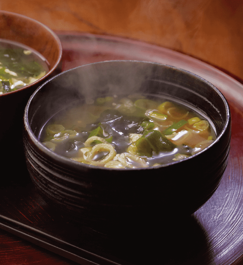 Miso soup with wakame seaweed and green onions served in a black bowl.