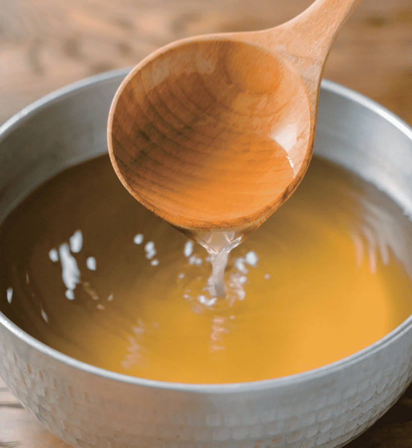 Golden corn dashi broth in a saucepan, with a wooden ladle lifting the rich, amber-colored stock.