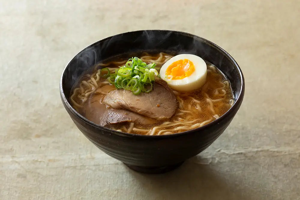 Bowl of Kayanoya Dashi ramen with sliced pork, egg, and green onions on a textured beige background