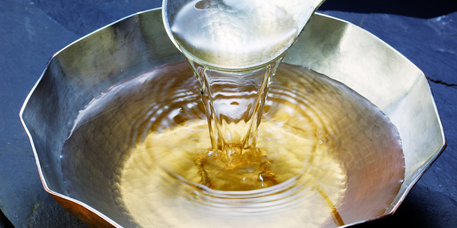 Clear dashi broth being ladled into a traditional metal bowl.
