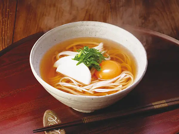 Bowl of Kayanoya Dashi and Soup for Udon with egg and green onions on a wooden table