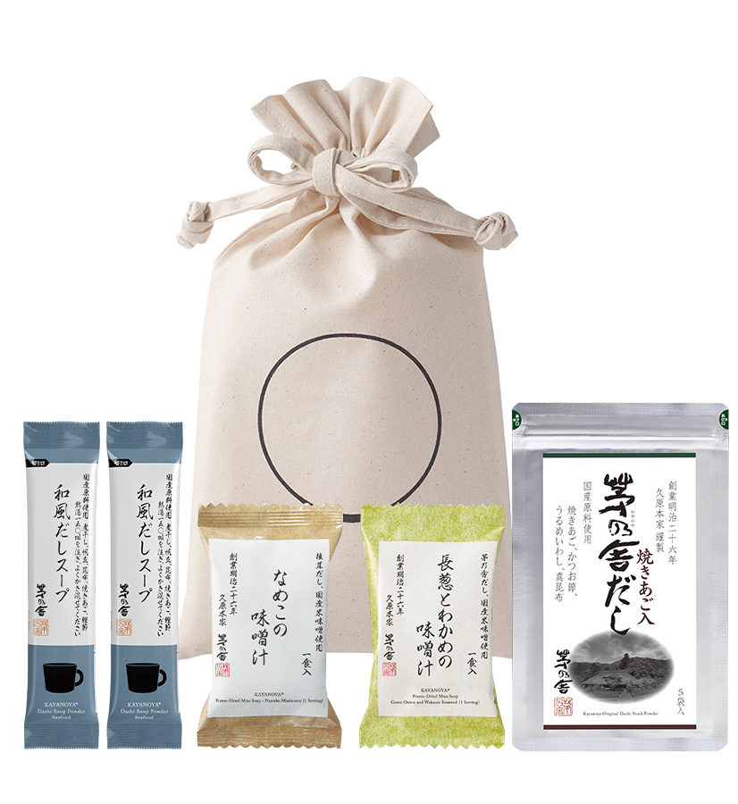 The Kayanoya Dashi Starter Kit - Original Dashi by Kayanoya USA features a beige drawstring bag with a circle design, two soup packets, dashi stock powder, snacks, and dried soup base—ideal as a Japanese cooking starter kit.