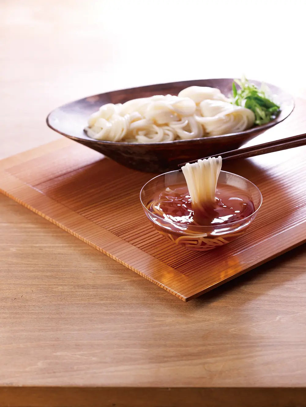 Bowl of Kayanoya Udon noodles with a small dish of dipping sauce on a wooden tray