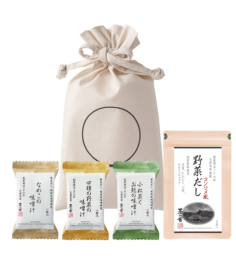 The Kayanoya Dashi Starter Kit - Vegetable Dashi by Kayanoya USA features a beige drawstring bag with Japanese text, three individually wrapped colorful snack packets, and a pink 野菜だし (vegetable stock powder) packet in front.