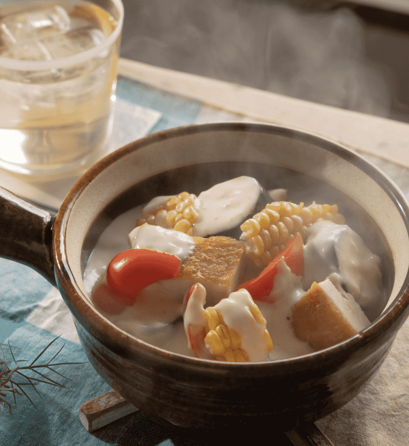 A steaming bowl of creamy chicken with corn, zucchini, cherry tomatoes, and red bell pepper in a light cream sauce.