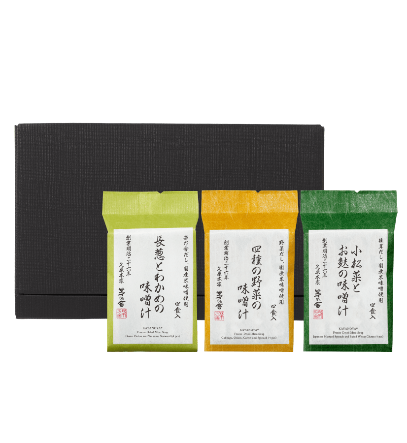A black Custom Umami Gift Box from Kayanoya USA sits behind three colorful packets of Freeze-Dried Soups, labeled in Japanese; the soups are green, yellow, and dark green from left to right.