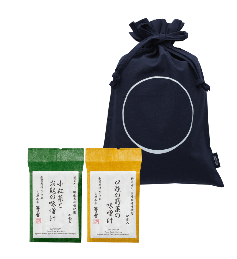 The Custom Umami Gift Bag - Medium from Kayanoya USA (Kubara Honke USA, Inc.) includes a navy organic cotton drawstring bag with a white circle and two Kayanoya Dashi Stock packets—one green-topped, one yellow-topped—with minimalist Japanese packaging.