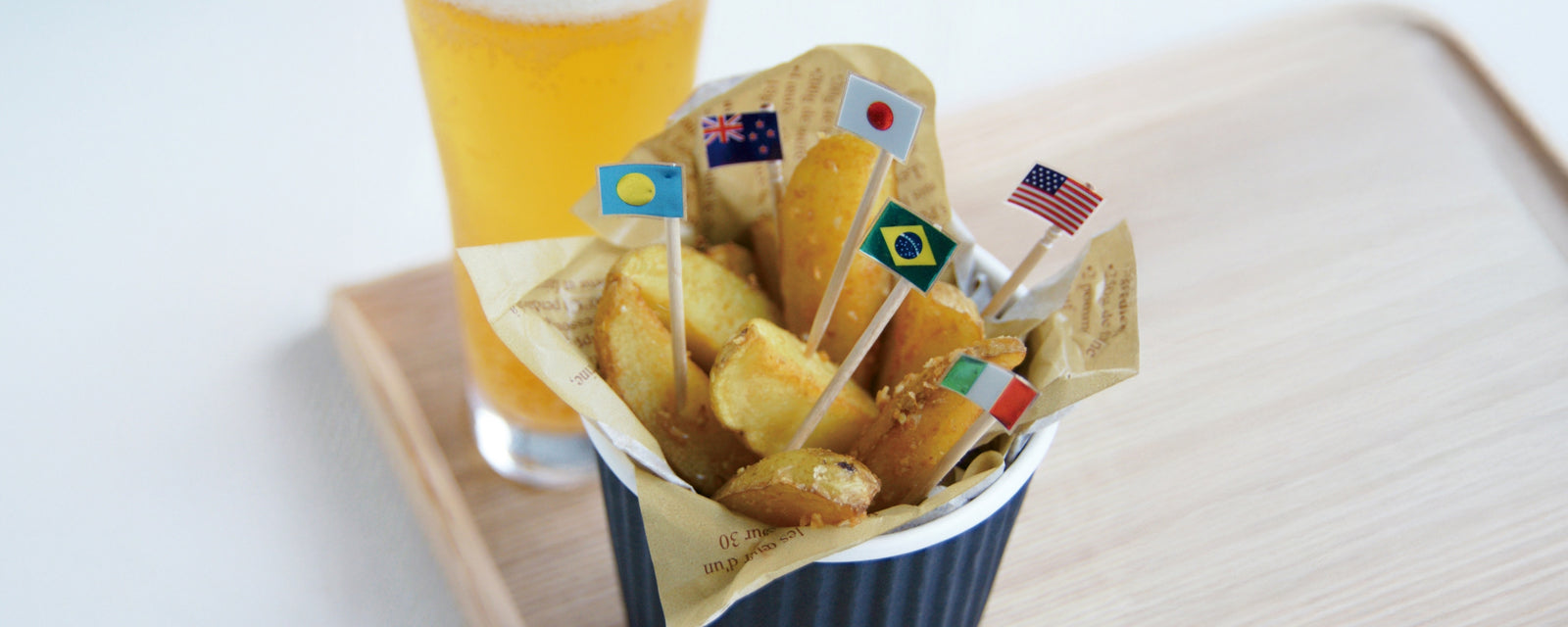 Fried potato wedges in a cup with small international flags, served with a glass of beer