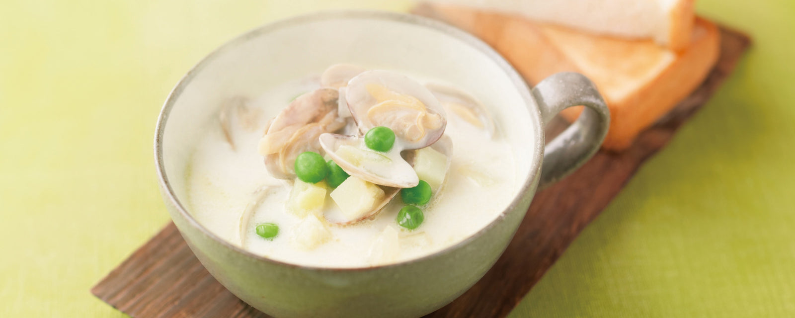 Creamy clam chowder with peas and potatoes in a cup, served with toasted bread.