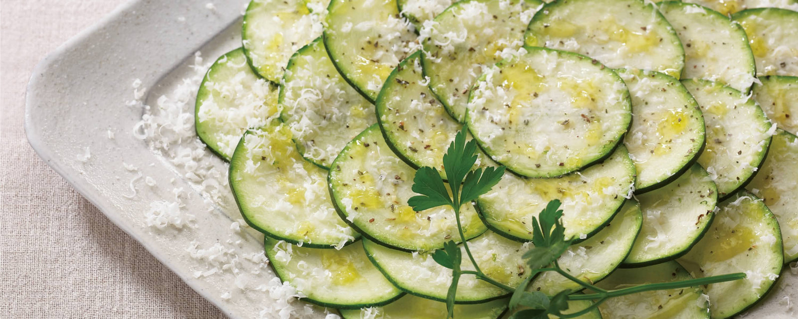 Thinly sliced zucchini carpaccio with olive oil, grated cheese, and fresh herbs on a plate.