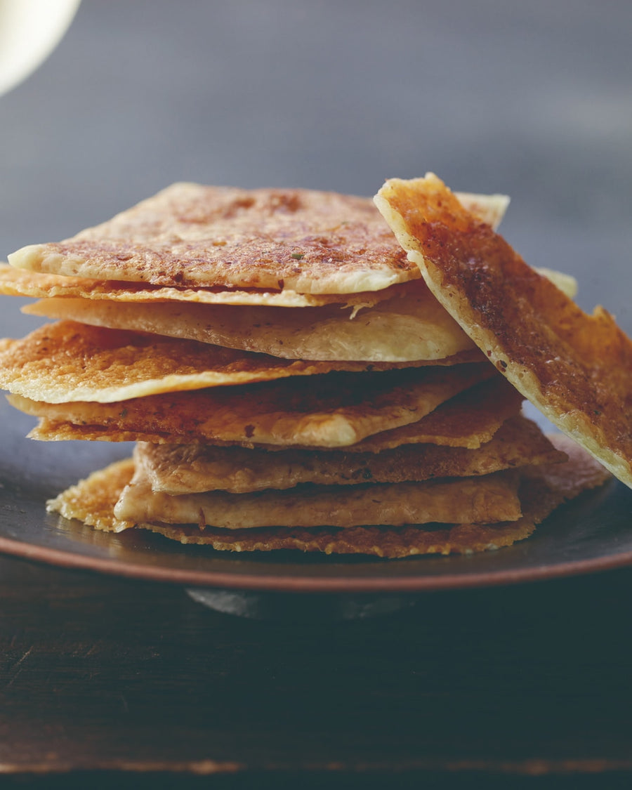 Crispy thin crackers stacked on a plate with a glass in the background.