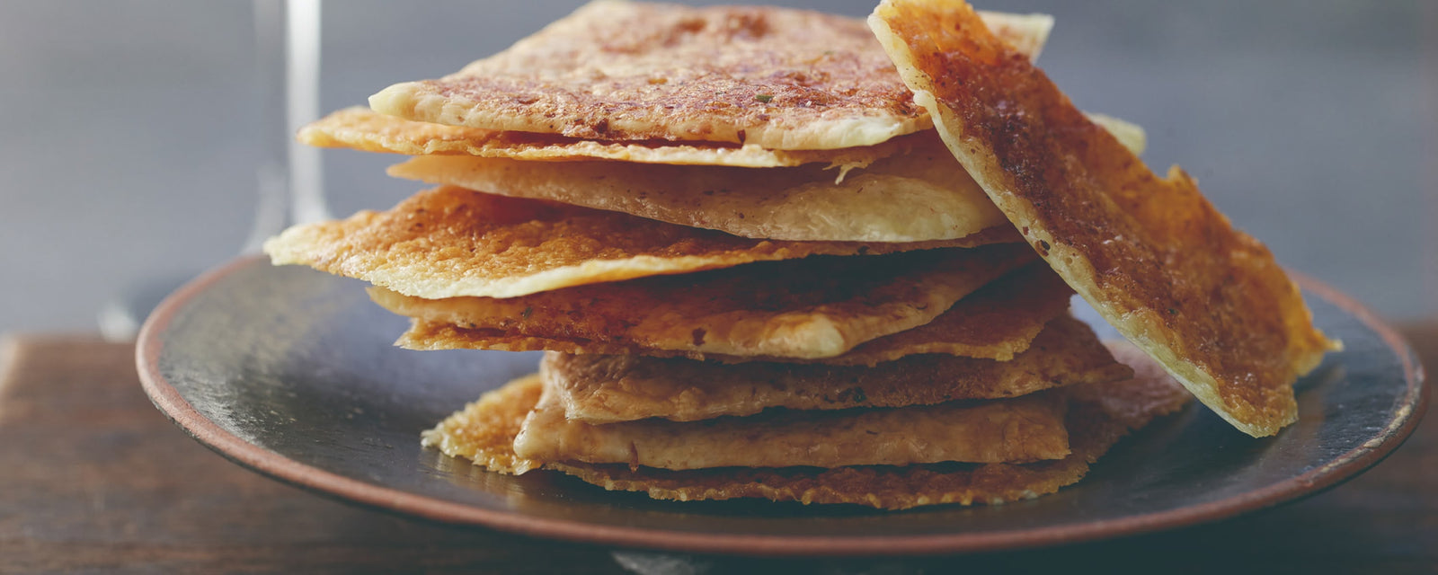 Crispy thin crackers stacked on a plate with a glass in the background.