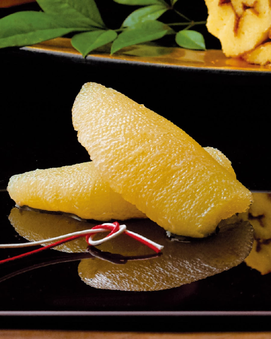 Kazunoko (seasoned herring roe), delicately marinated and served as a traditional Japanese New Year delicacy, presented on a glossy black plate with decorative red and white mizuhiki cord.