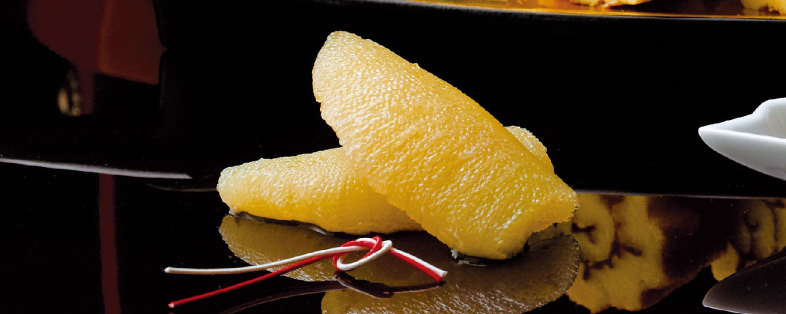 Kazunoko (seasoned herring roe), delicately marinated and served as a traditional Japanese New Year delicacy, presented on a glossy black plate with decorative red and white mizuhiki cord.