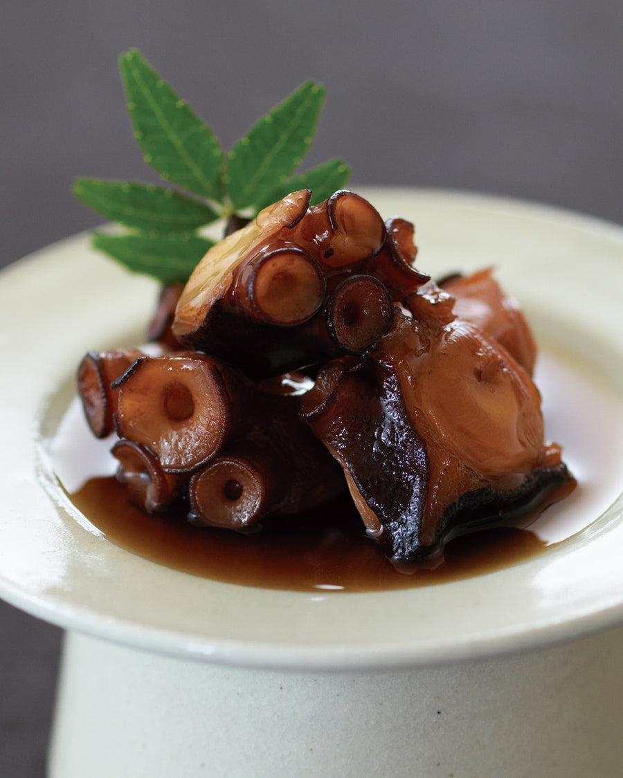 Simmered octopus pieces glazed in a sweet soy-based sauce, served as a traditional Japanese appetizer with a garnish leaf.