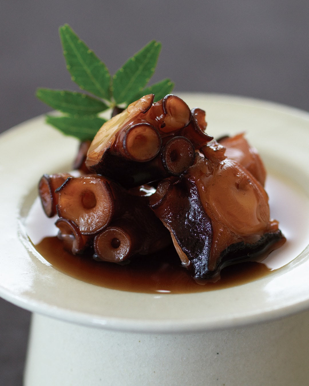 Simmered octopus pieces glazed in a sweet soy-based sauce, served as a traditional Japanese appetizer with a garnish leaf.
