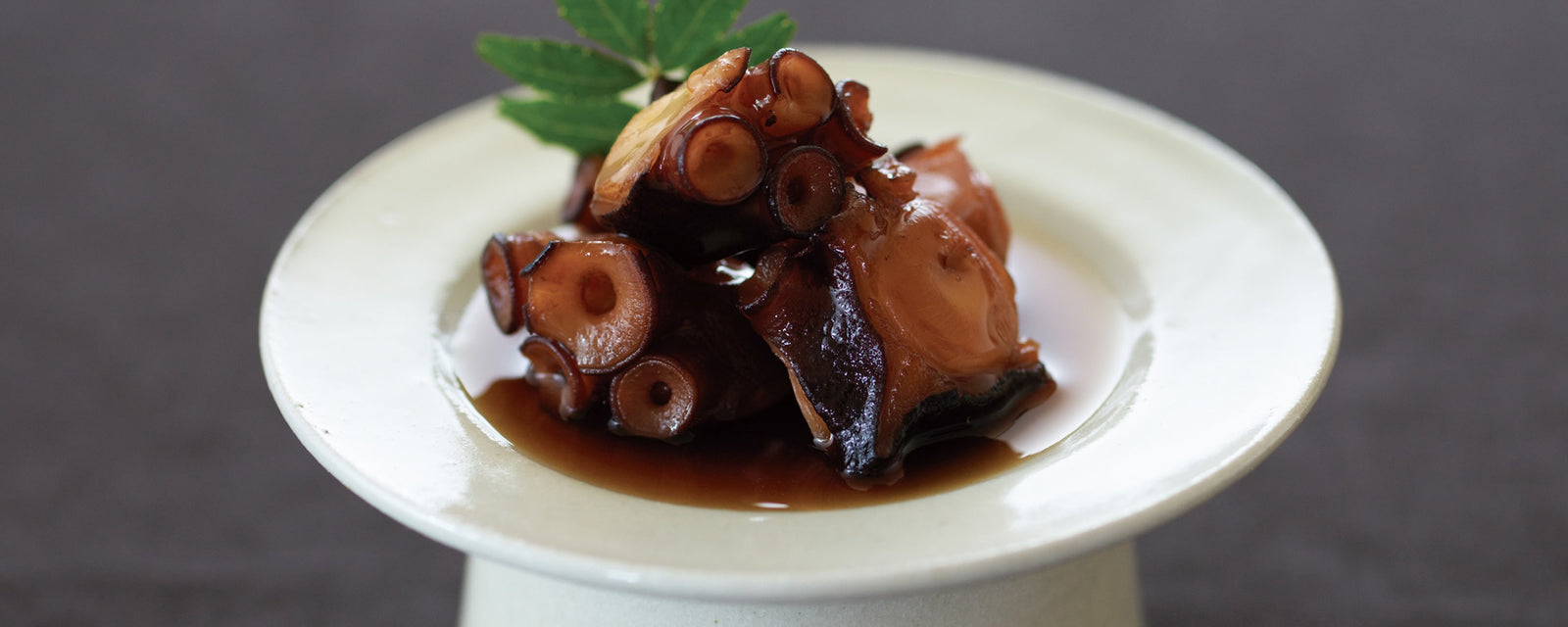 Simmered octopus pieces glazed in a sweet soy-based sauce, served as a traditional Japanese appetizer with a garnish leaf.