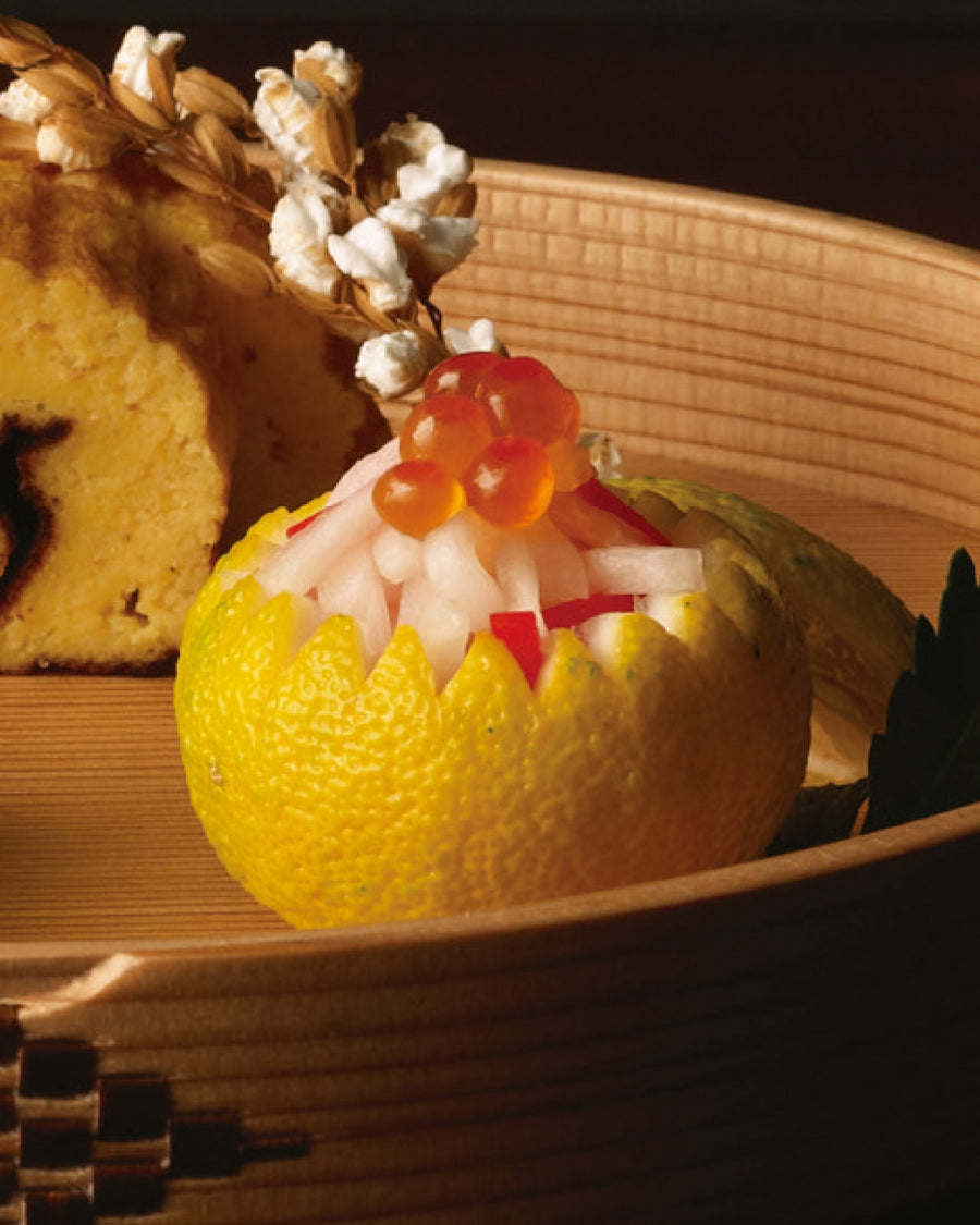 A carved citrus fruit cup filled with daikon strips and topped with salmon roe, served on a wooden plate.