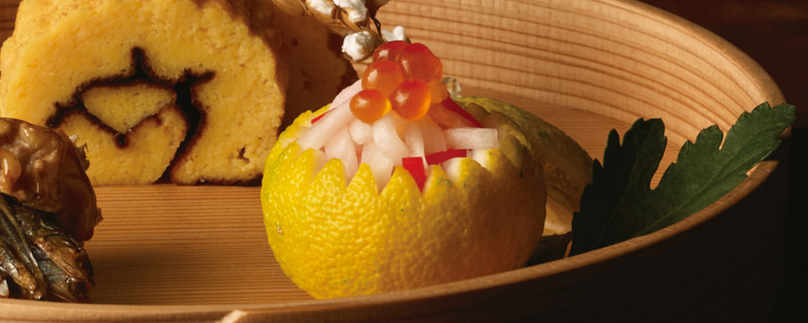 A carved citrus fruit cup filled with daikon strips and topped with salmon roe, served on a wooden plate.