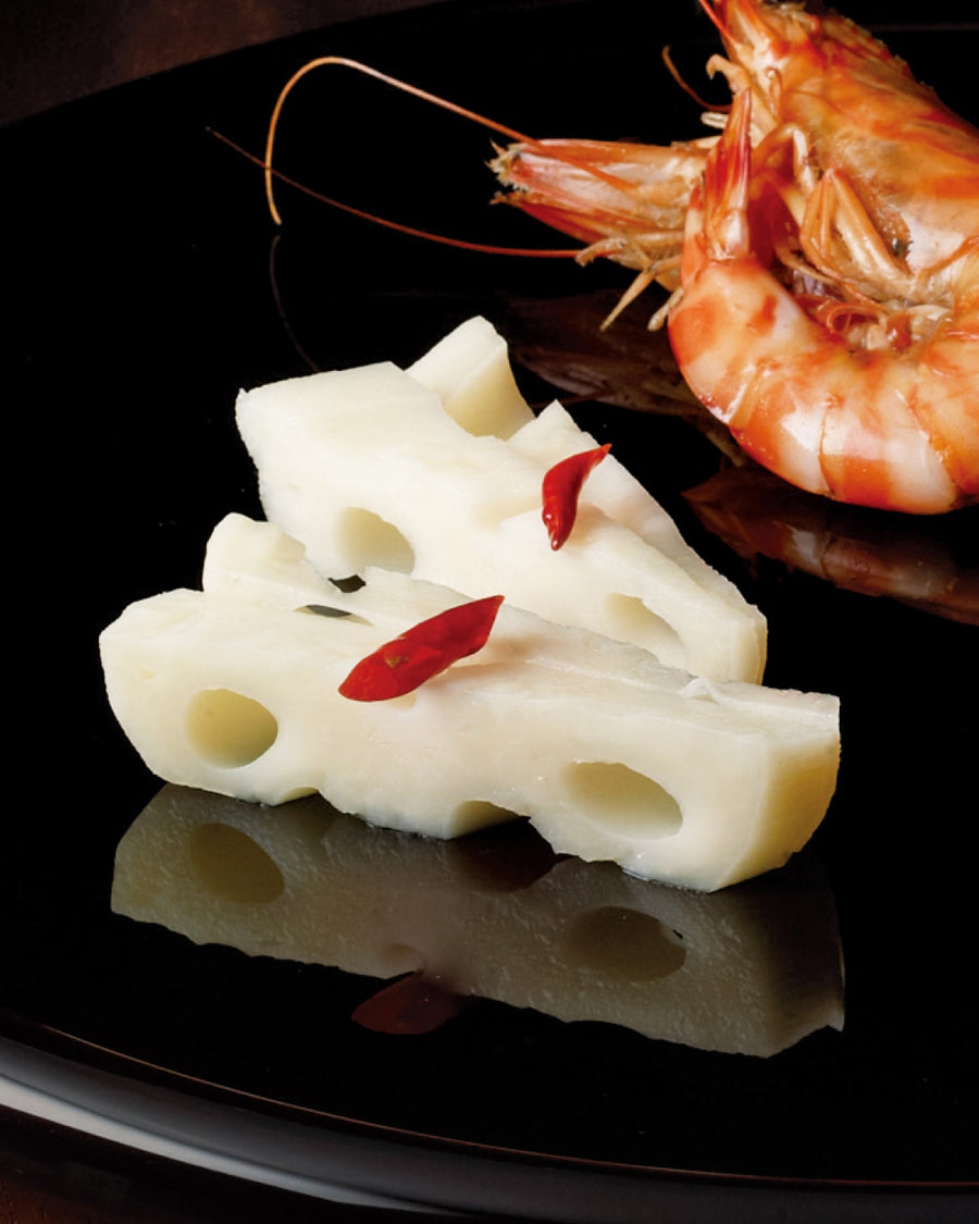 Slices of lotus root topped with small red chili pieces, served on a glossy black plate alongside shrimp.