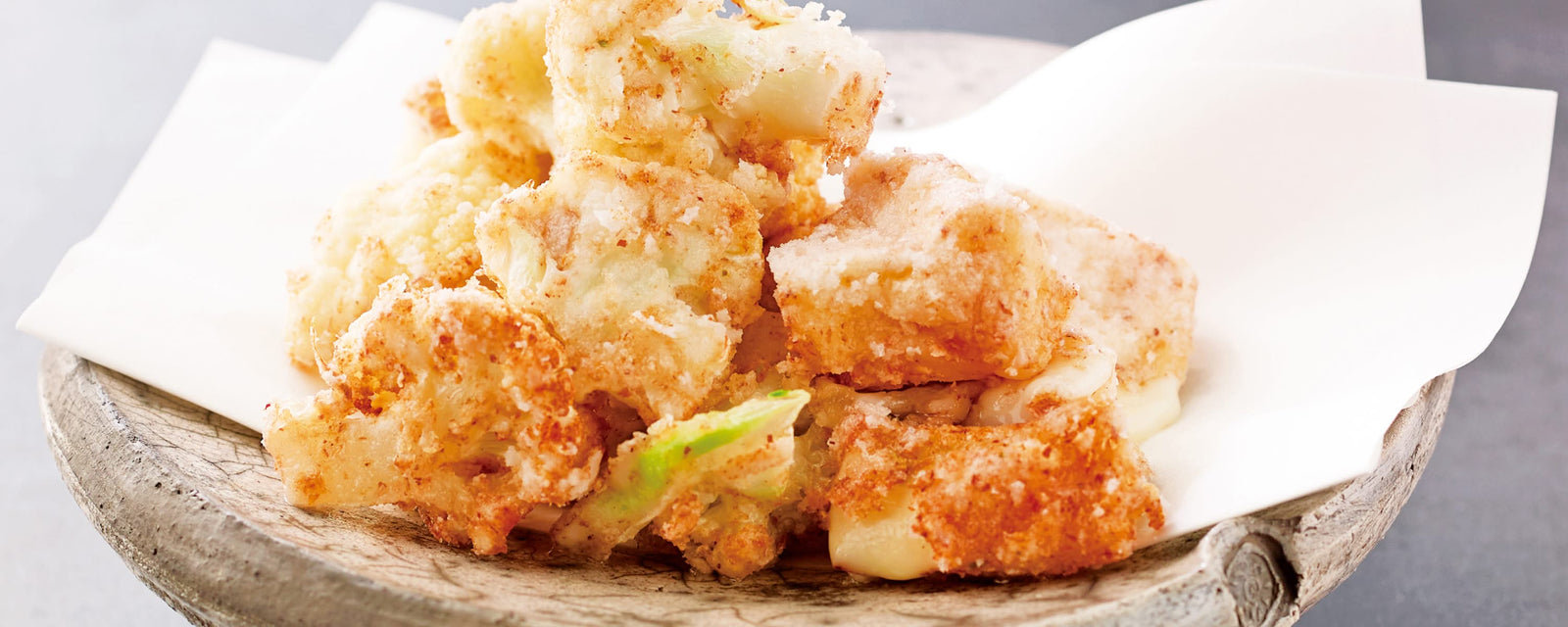 Golden, crispy battered cauliflowers served on parchment paper atop a rustic wooden plate.