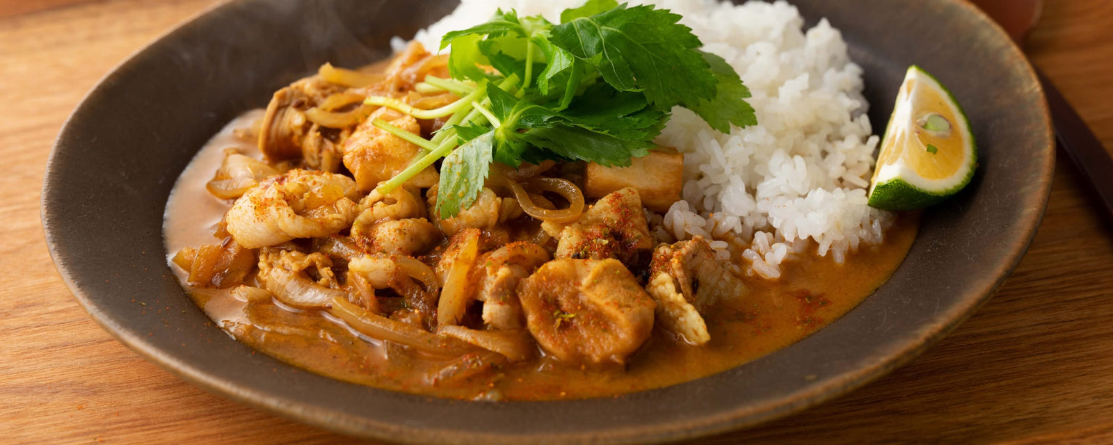 Pork, wheat gluten and onion curry served with steamed white rice, topped with fresh herbs and a lime wedge.