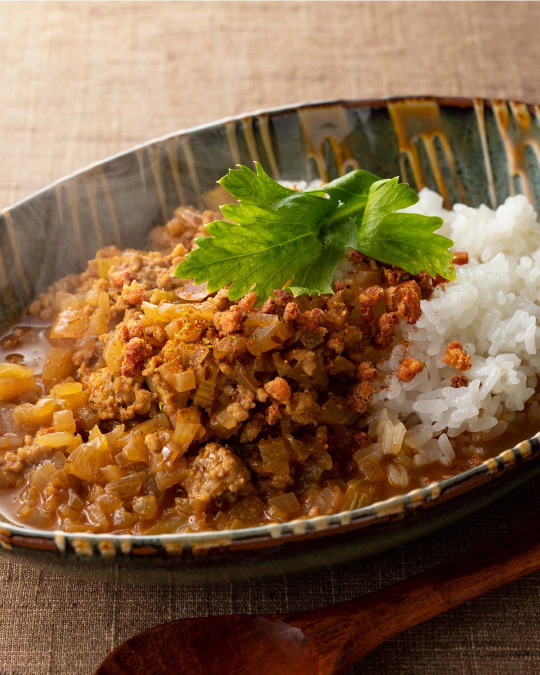 Minced meat and onion curry served over white rice, garnished with fresh green herb leaves.