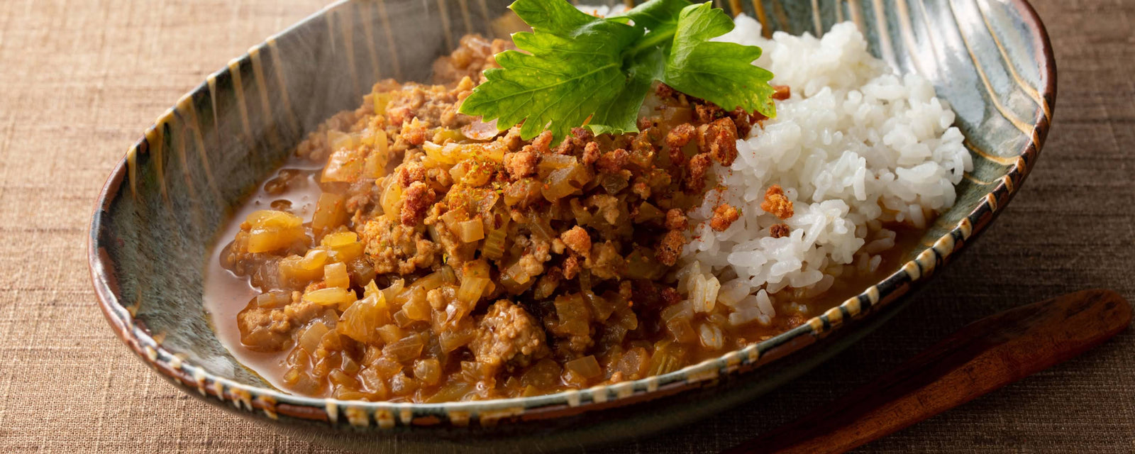 Minced meat and onion curry served over white rice, garnished with fresh green herb leaves.
