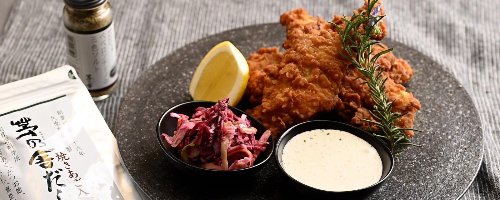 Crispy fried chicken pieces served with lemon wedge, rosemary garnish, creamy dipping sauce, and a side of purple cabbage slaw.