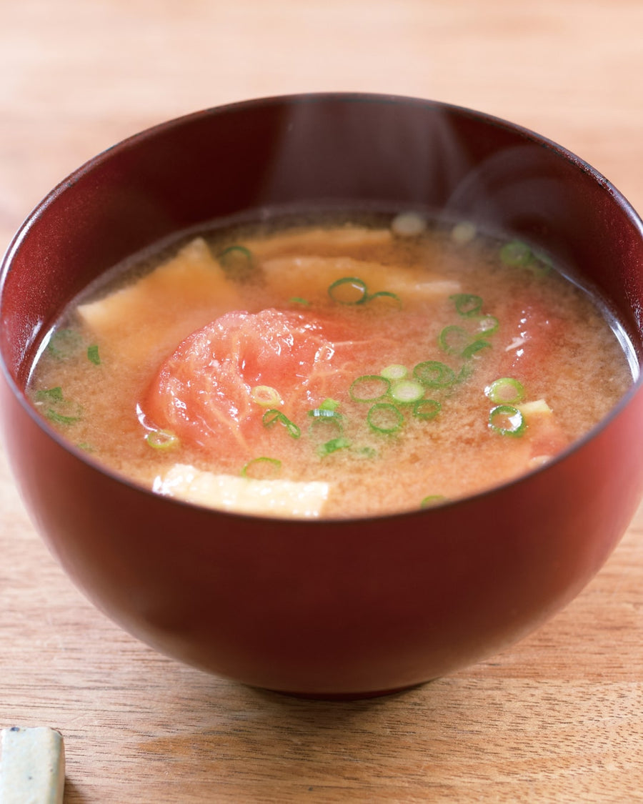 Miso soup with tomato, tofu cubes, and sliced green onions in a red bowl.