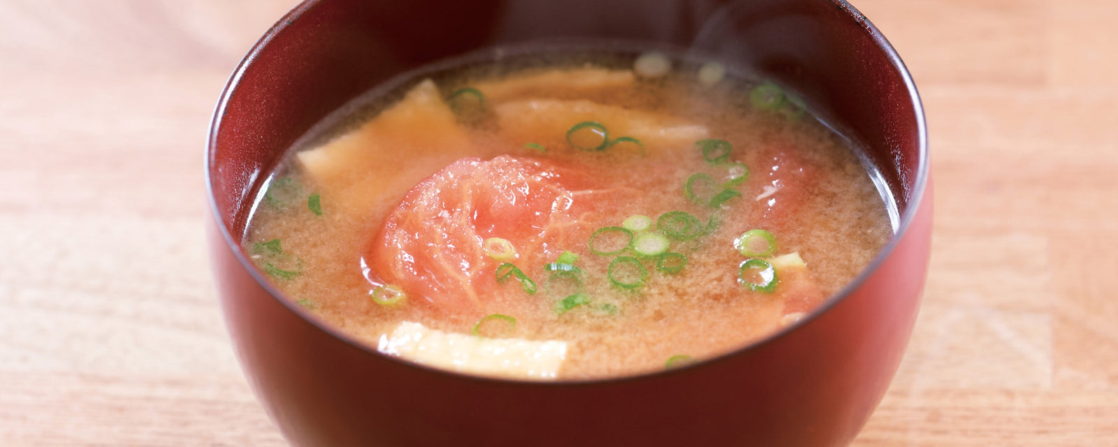 Miso soup with tomato, tofu cubes, and sliced green onions in a red bowl.