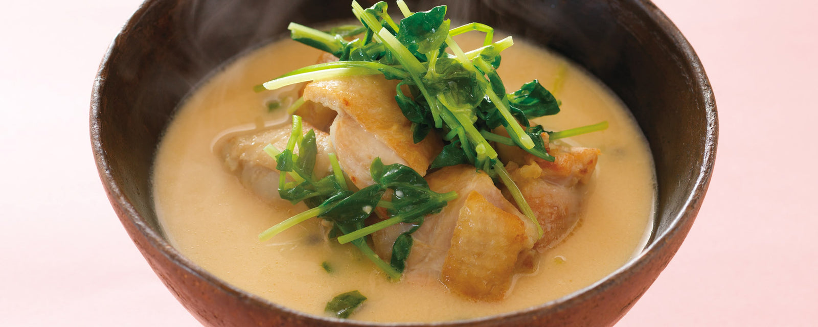Creamy miso soup with tender chicken pieces, topped with fresh greens in a rustic bowl.