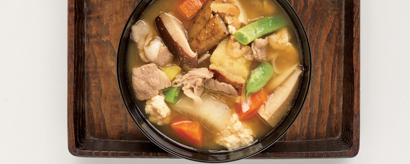 Hearty pork miso soup with chunky vegetables, tofu, and mushrooms served in a black bowl on a wooden tray.