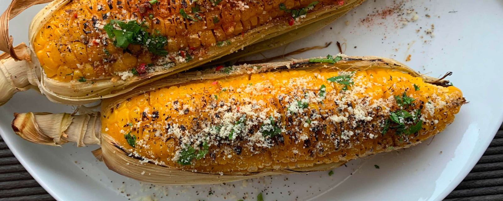 Grilled corn on the cob topped with grated cheese and herbs