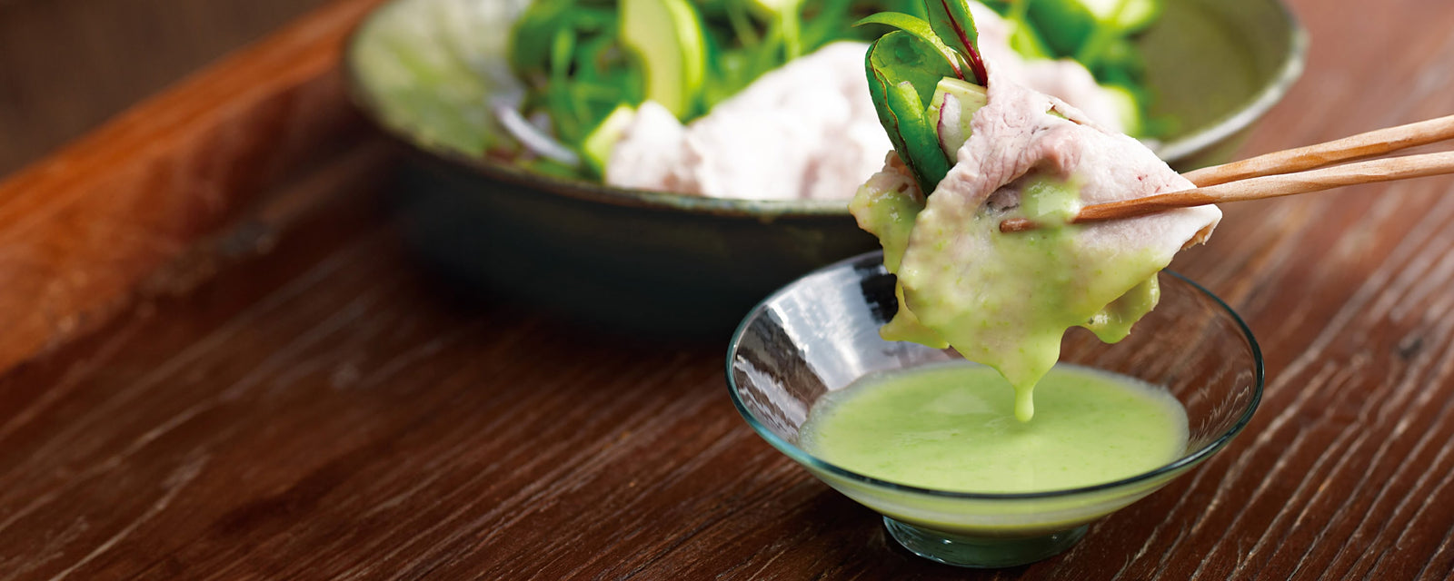 Pork and vegetables dipped into a light green edamame shabu-shabu sauce in a small glass bowl.