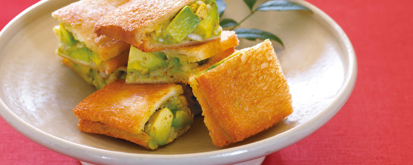 Crispy avocado pocket sandwiches with golden toasted bread and avocado filling stacked on a ceramic plate.