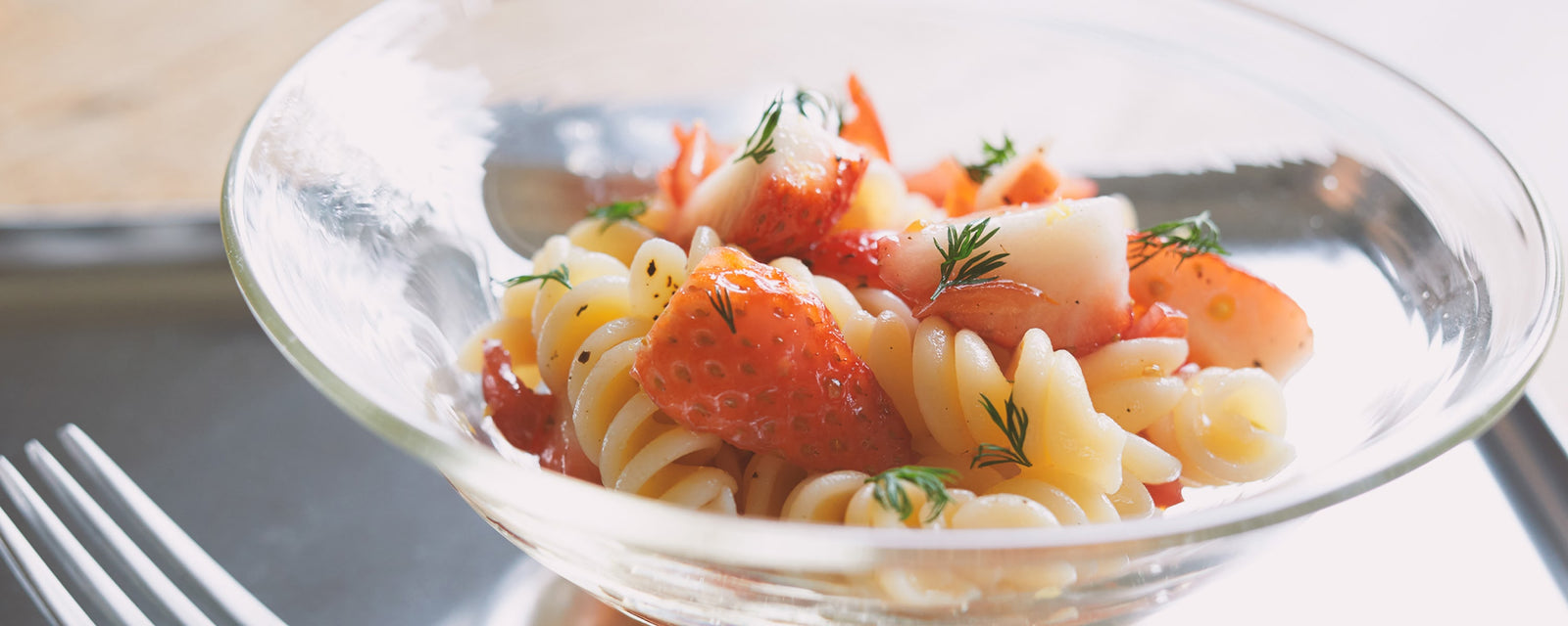 Strawberry pasta salad with spiral noodles, fresh strawberry pieces, and herb garnish served in a clear glass bowl.