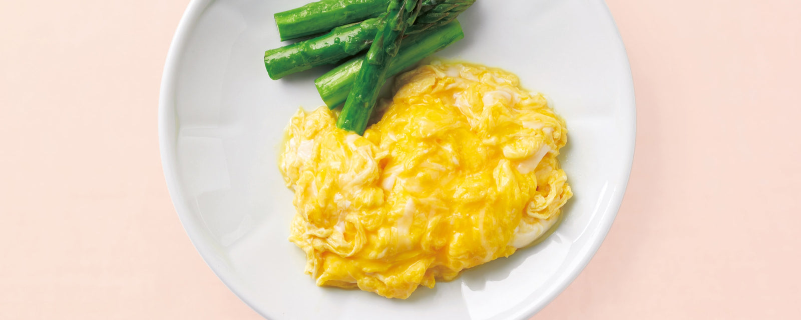 Soft scrambled eggs served on a white plate with green asparagus spears.