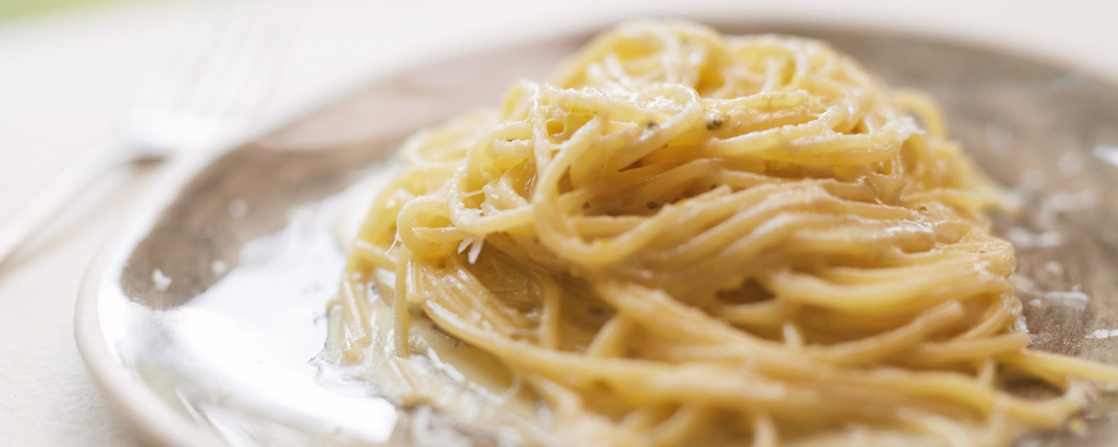 Creamy lemon pasta with spaghetti coated in a light sauce and grated cheese on a plate.