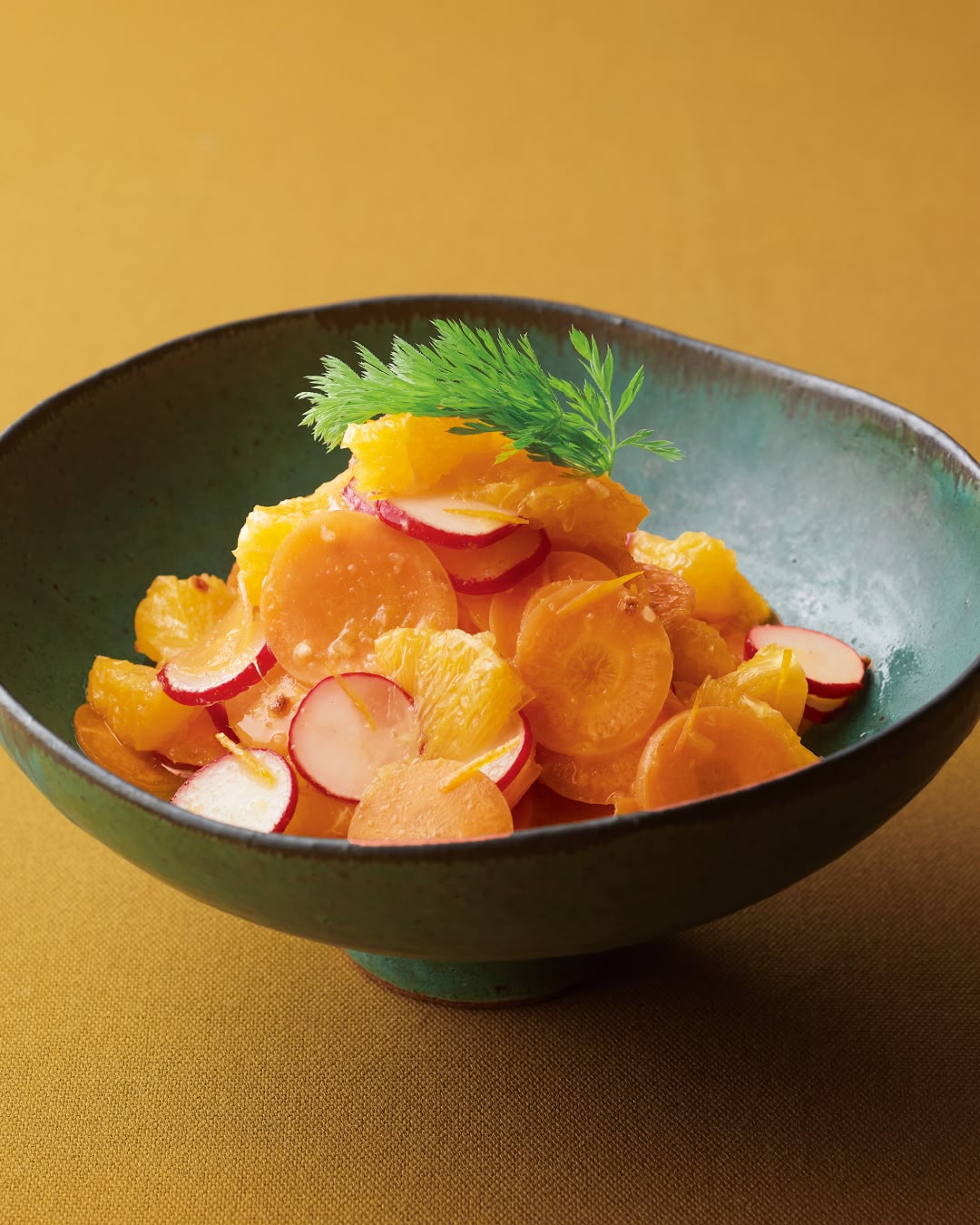 A bowl of orange salad with sliced carrots, radishes, and orange segments, garnished with fresh herbs.
