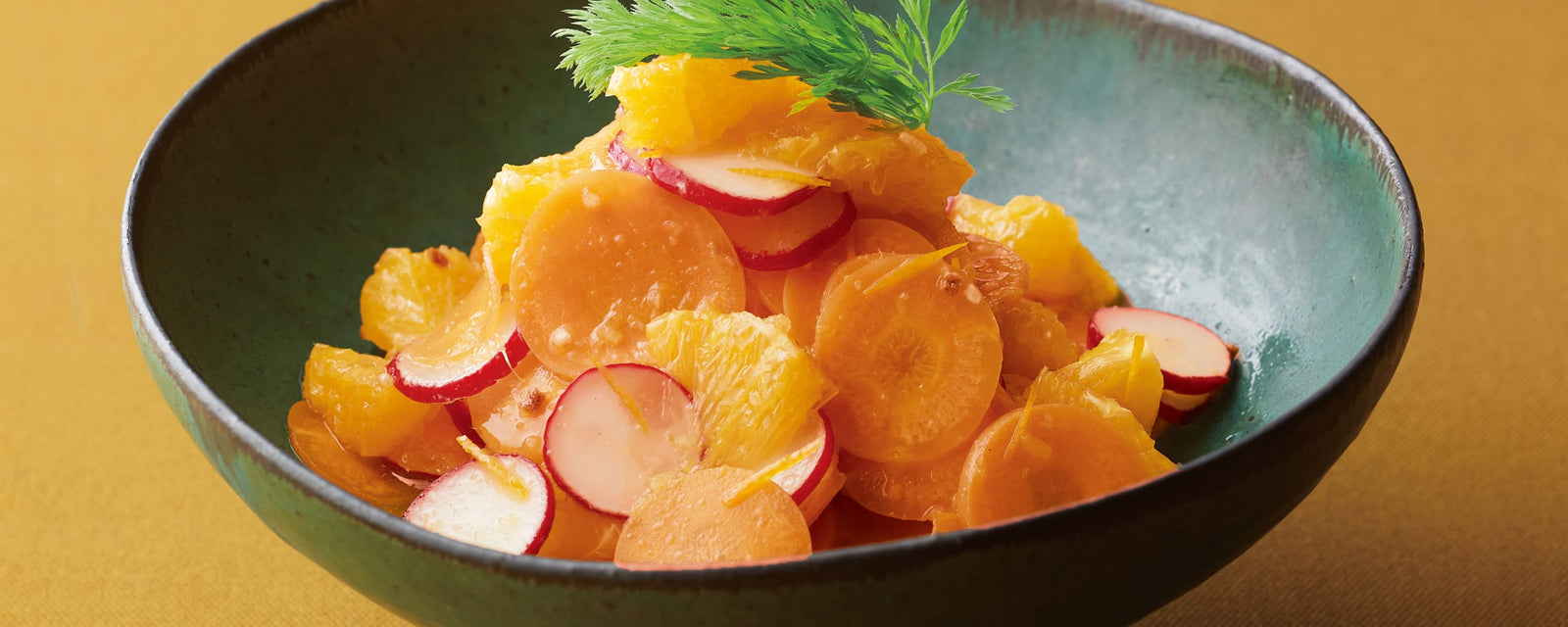 A bowl of orange salad with sliced carrots, radishes, and orange segments, garnished with fresh herbs.