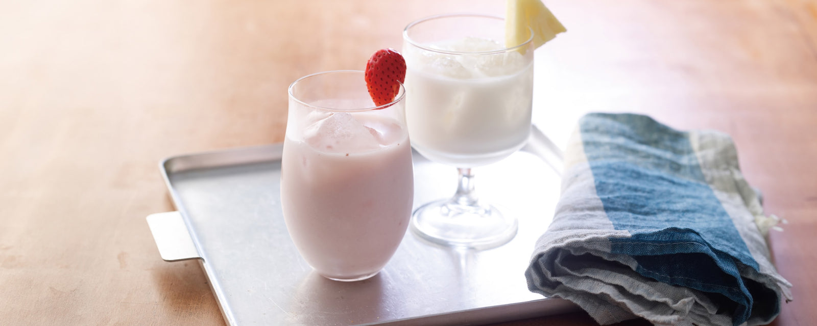 A glass of grape lassi and a glass of yuzu lassi with ice, served on a metal tray with a cloth napkin.