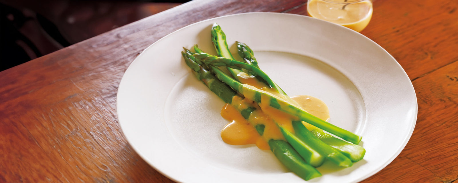 Asparagus with a umami hollandaise sauce on a white plate on a wooden table.