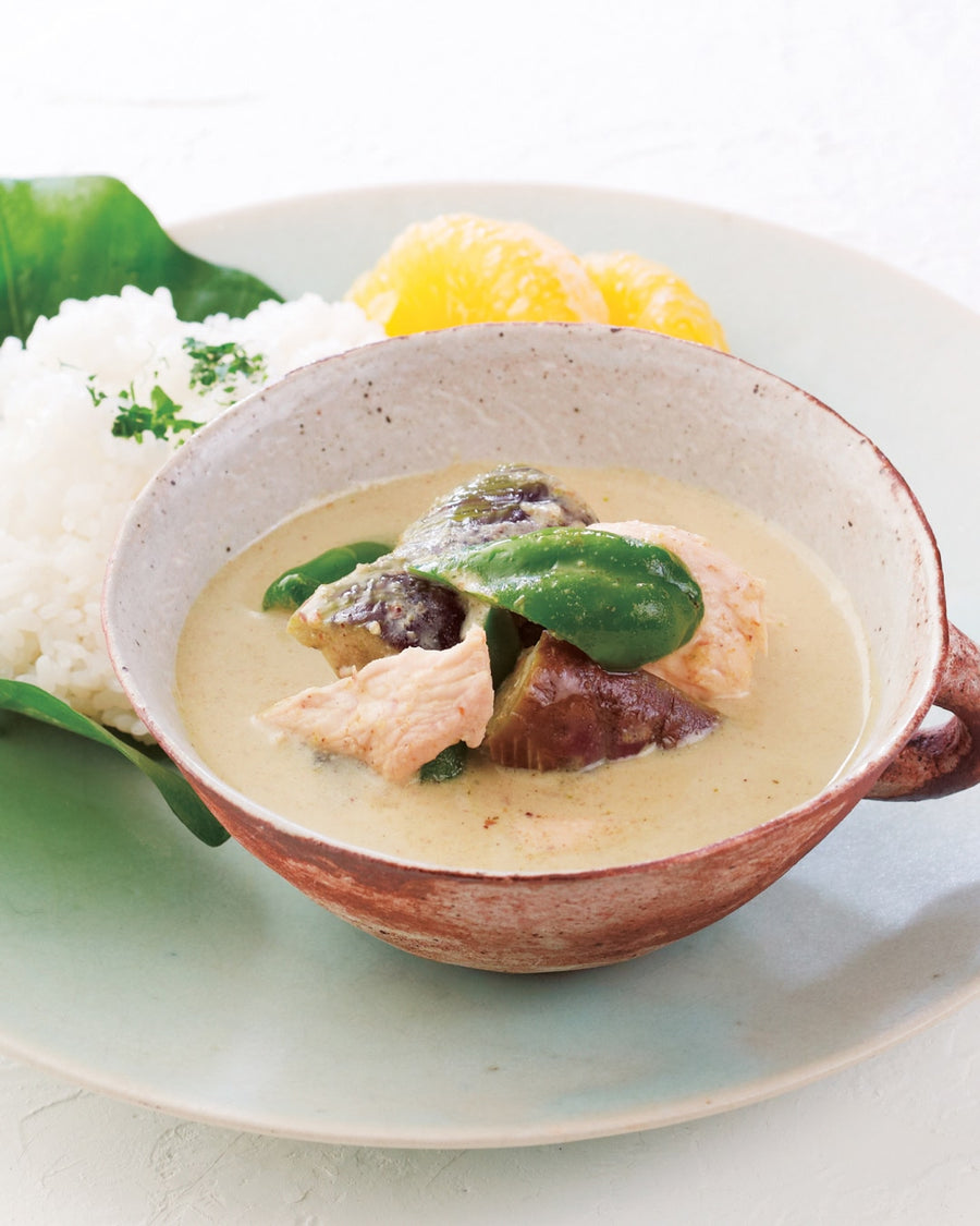 Bowl of creamy chicken green curry with rice and vegetables on a white plate