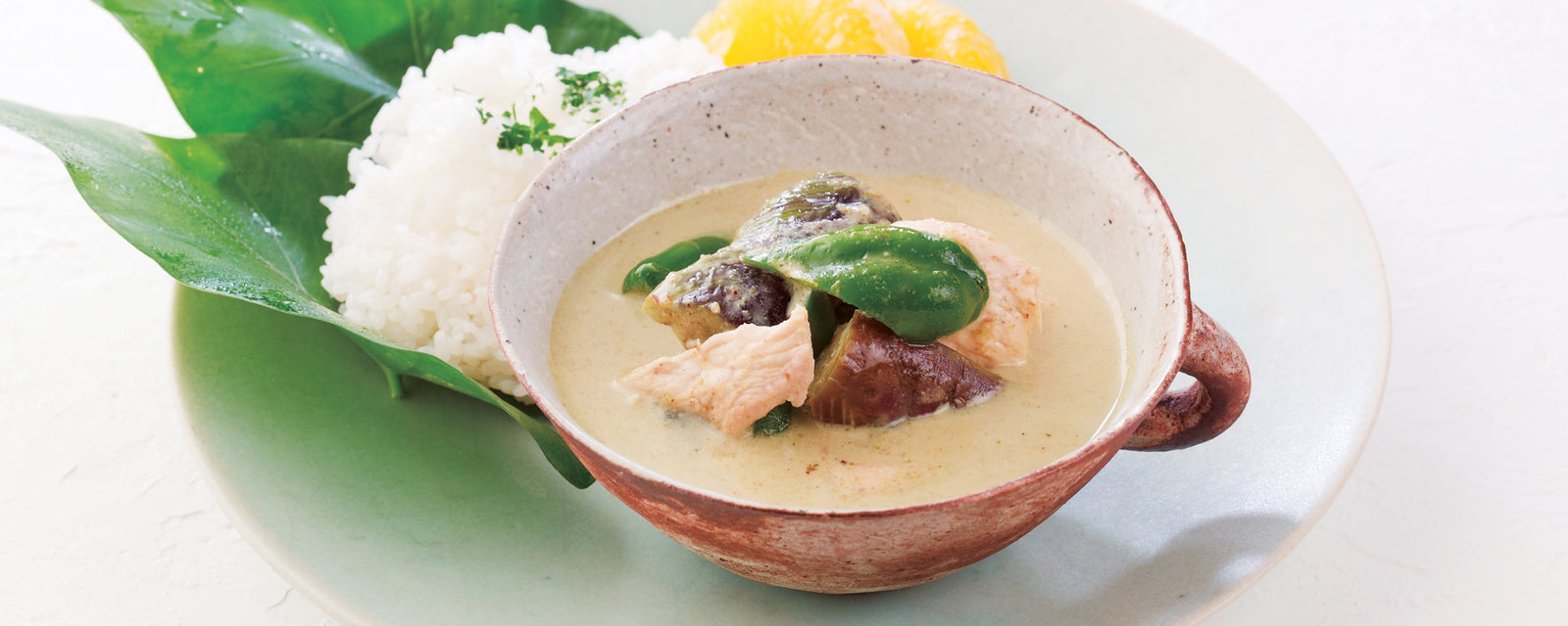 Bowl of creamy chicken green curry with rice and vegetables on a white plate