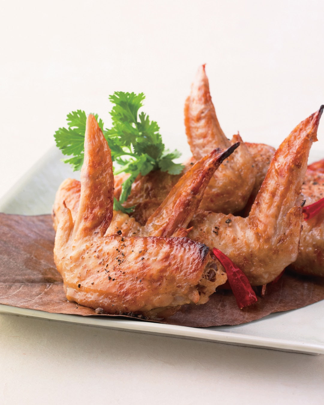A plate of Thai-inspired coconut dashi chicken wings garnished with herbs and dried chili.
