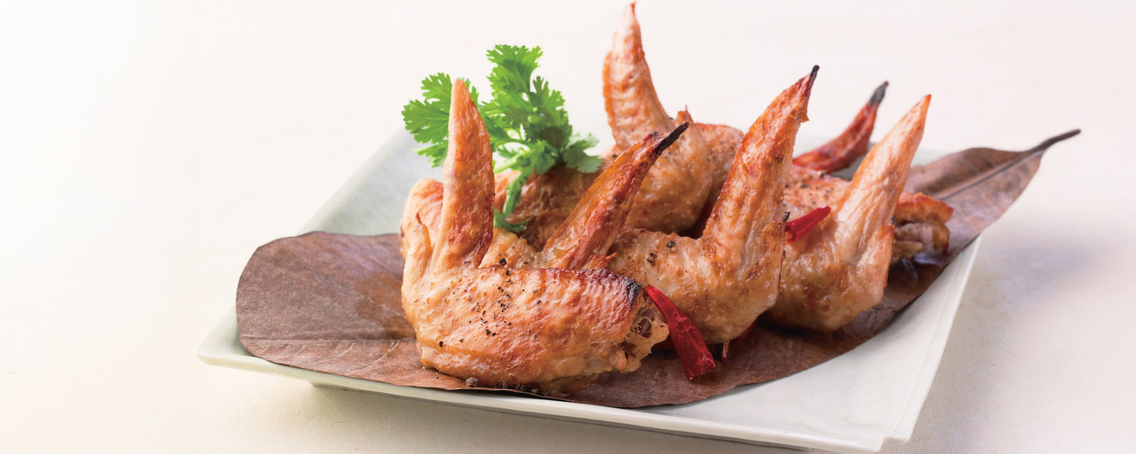A plate of Thai-inspired coconut dashi chicken wings garnished with herbs and dried chili.