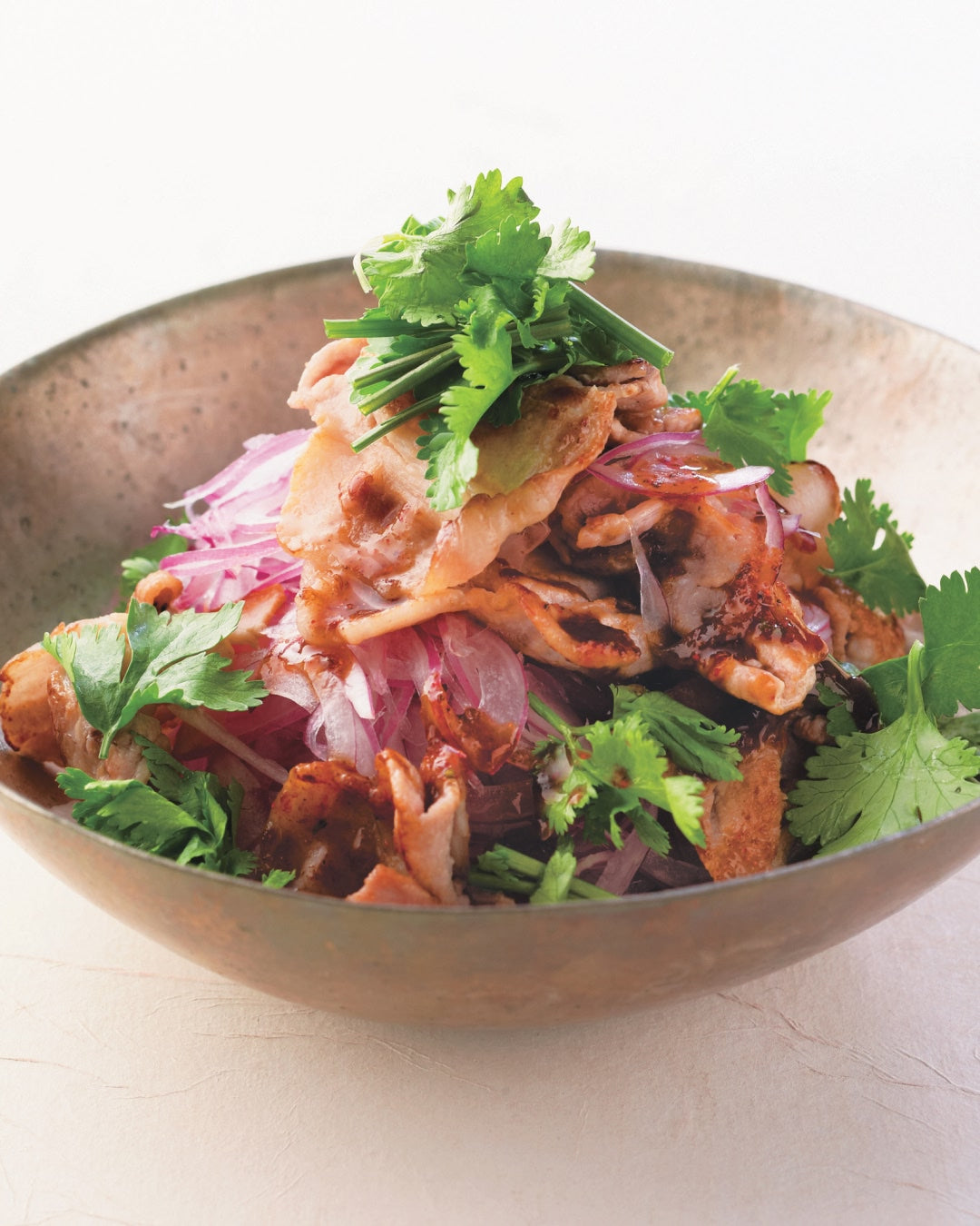A bowl of Thai-inspired spicy dashi pork salad with red onions and fresh cilantro.